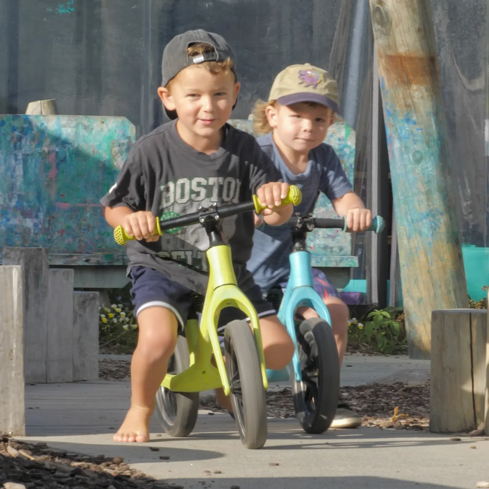 Two boys in caps sitting on balance bikes side by side, grinning at the camera.