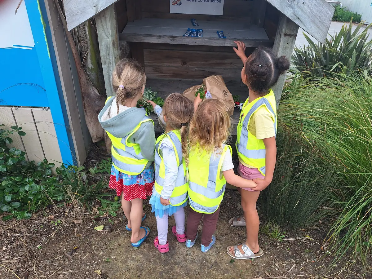 Four children in hi-vis vests looking into a wooden bug hotel filled with plants and paper bags.